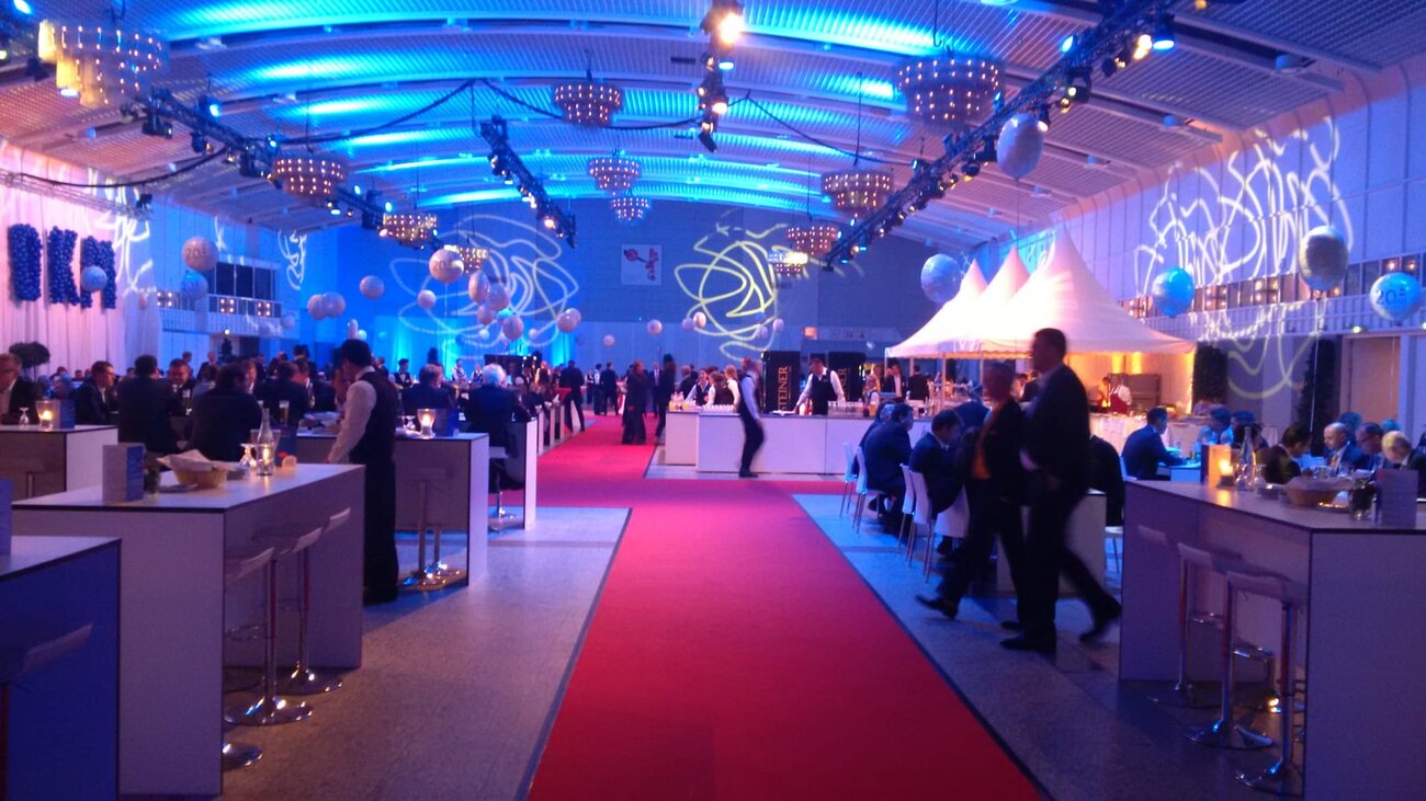 Get-together in Halle 1 mit Stehtischen, Tanzfläche und atmosphärischer Beleuchtung.